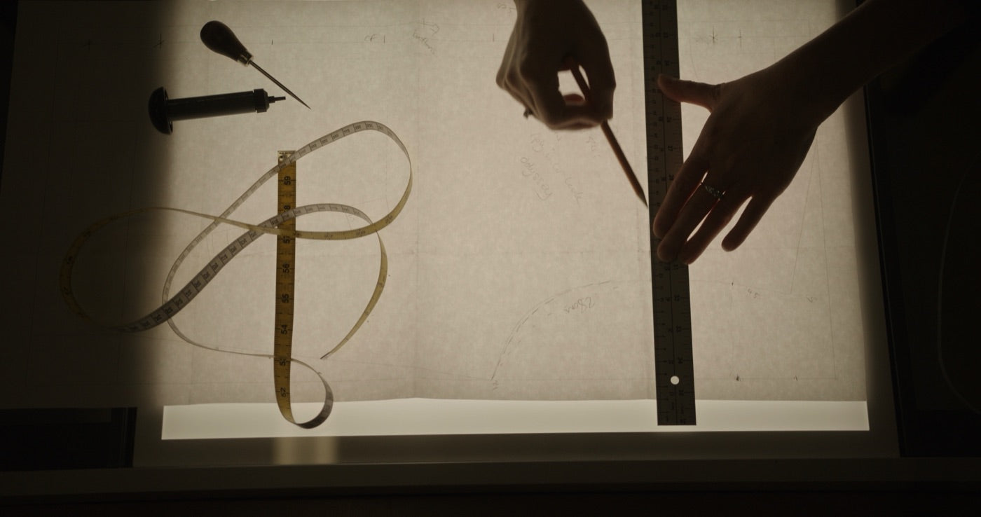 Hands drawing a pattern with ruler and pencil on a light box, a tape measure beside them
